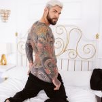 sexy Latino with body covered in tattoos pulls down pants