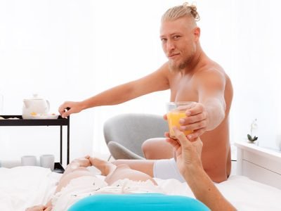 Blonde male actor hands woman a glass of orange juice.