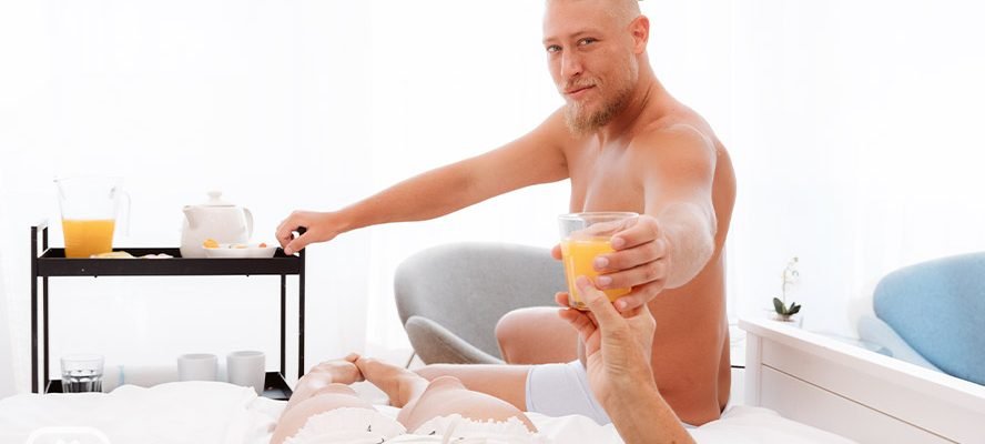 Blonde male actor hands woman a glass of orange juice.