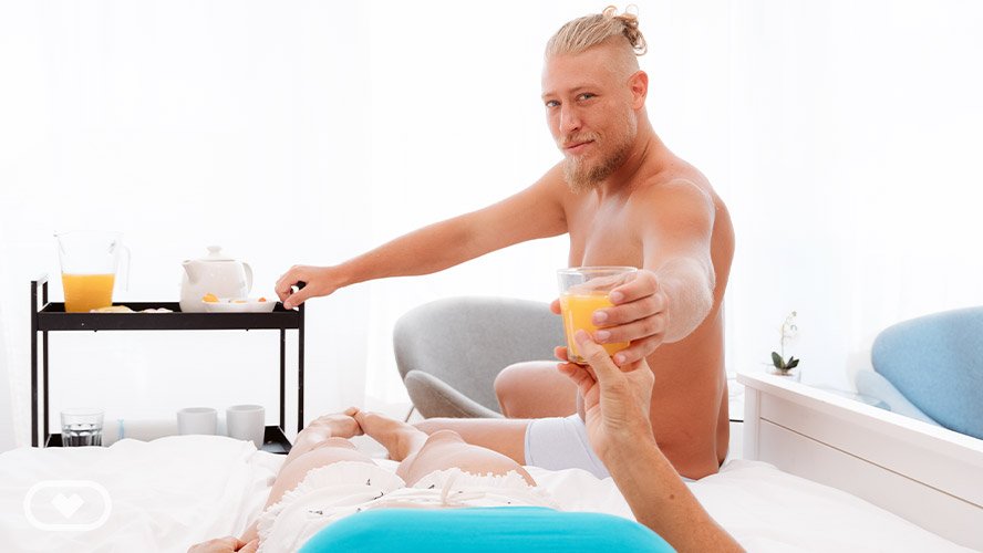 Blonde male actor hands woman a glass of orange juice.